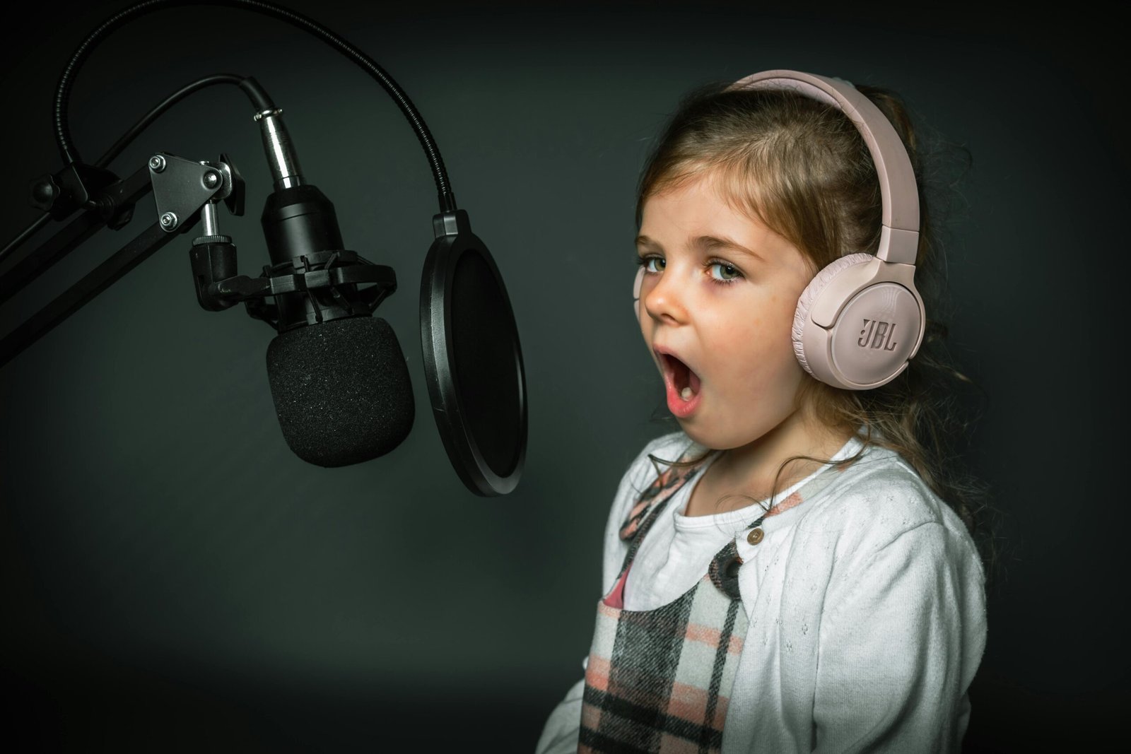 A young girl in a recording studio sings into a microphone wearing headphones.